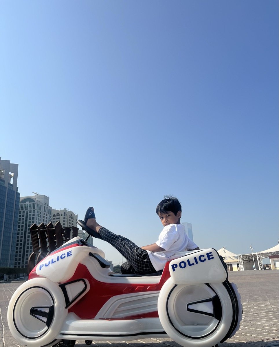 Dhyanchand kicking his leg up on a police-style ride-on toy with city skyline
